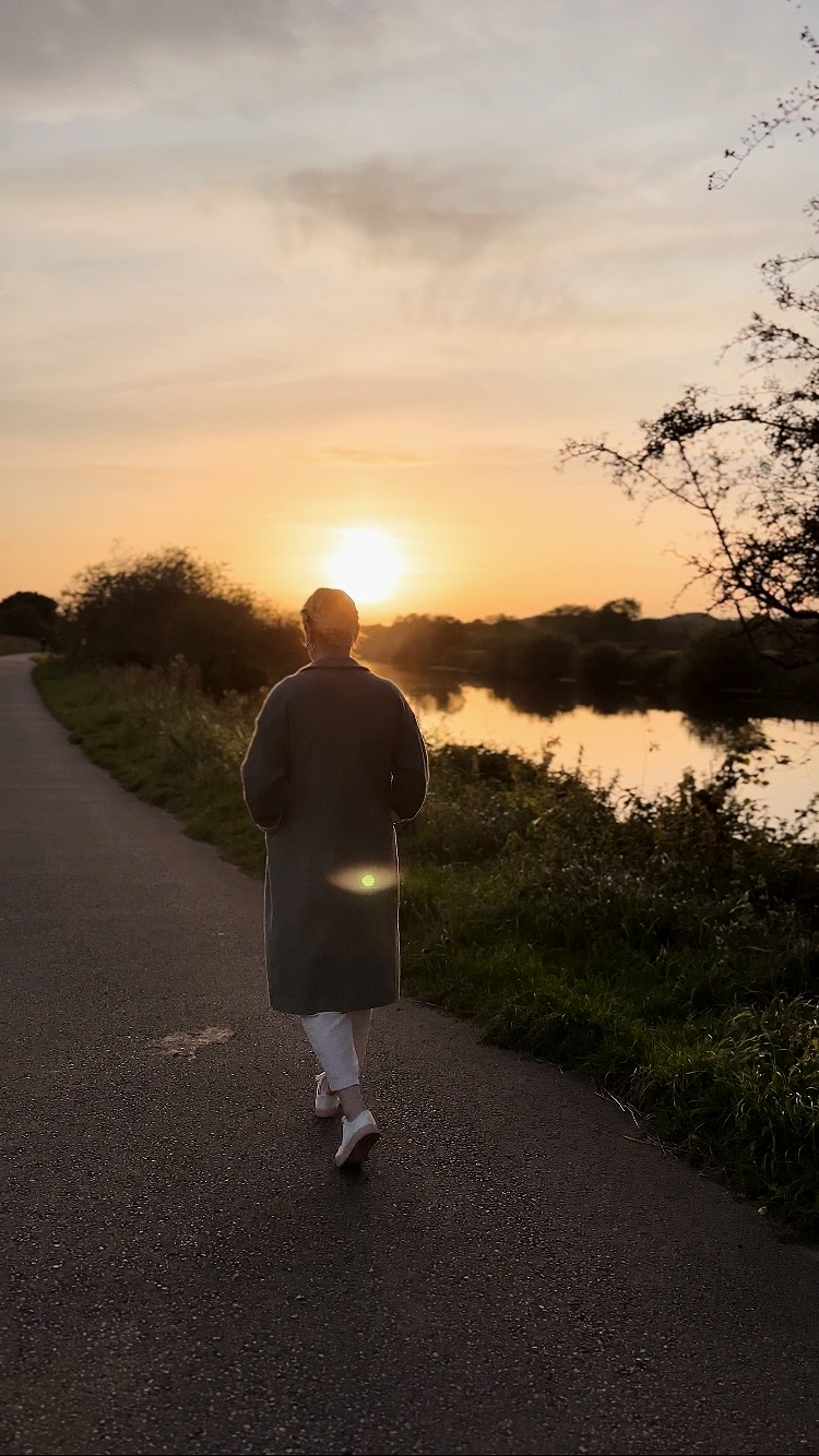 Amy is walking away, silhouetted against a sunset next to a river